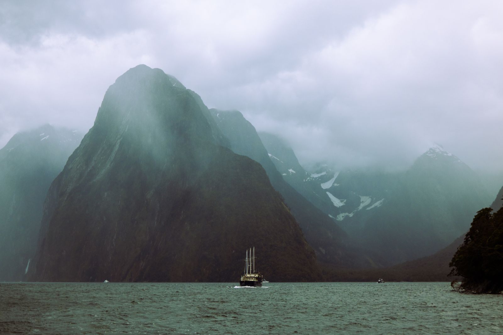 Small sailing boat beneath misty peaks in Milford Sound, scenery on small ship cruises to Australia and New Zealand